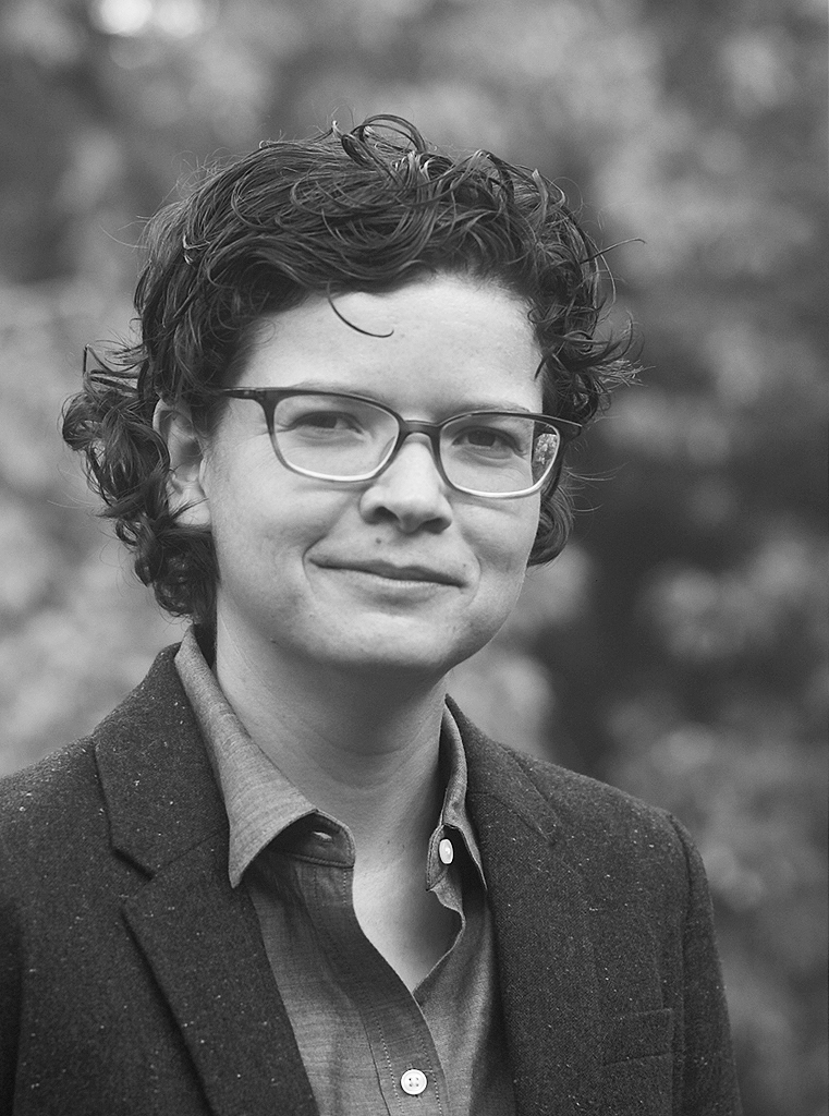 Black and white photo of Dr. Banazek wearing glasses and a gray blazer, in front of trees