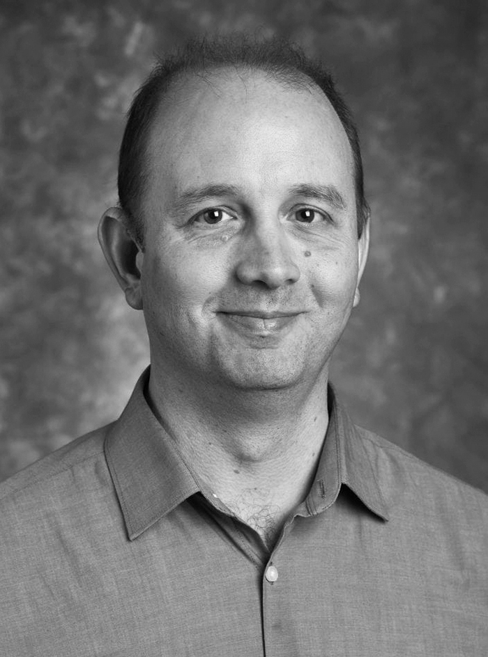 Black and white studio photo of Dr. Magrane wearing a button-down shirt.